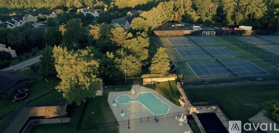 An aerial view of a tennis court surrounded by trees and a swimming pool.