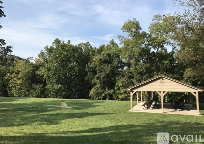 A wooden pavilion is situated in a grassy field with trees in the background.