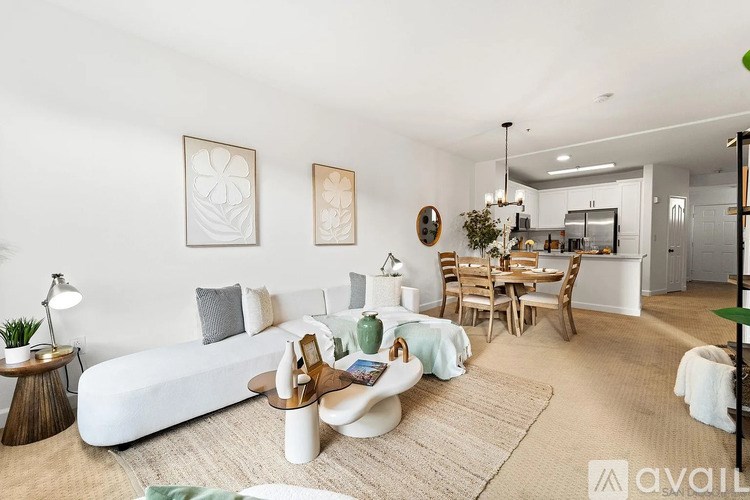 A modern living room with a white sofa, a wooden coffee table, and a dining area in the background.