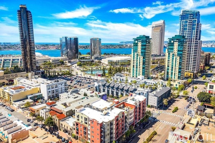 A cityscape with a mix of modern and older buildings, a clear sky, and a body of water in the distance.