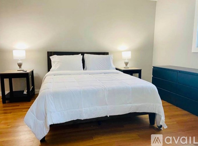 A bed with white bedding is in a room with wooden floors and two nightstands with lamps.