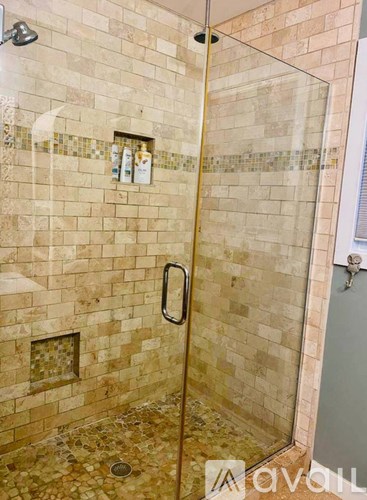 A shower with a glass door and tiled walls.