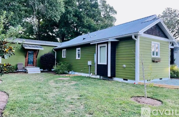 A green house with a black door and a small tree in the front yard.