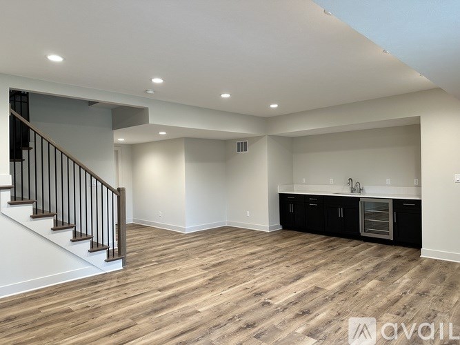 A spacious room with wooden flooring and a staircase with black railings.