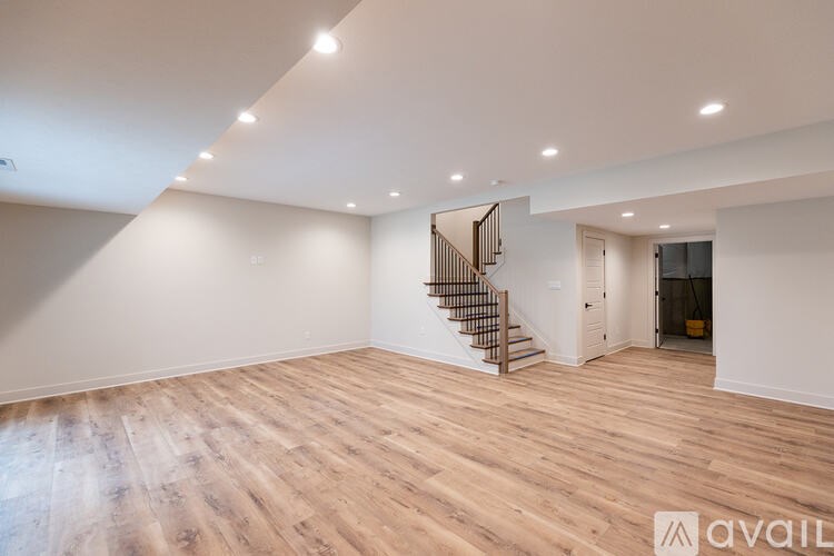 A spacious room with wooden flooring and a staircase.
