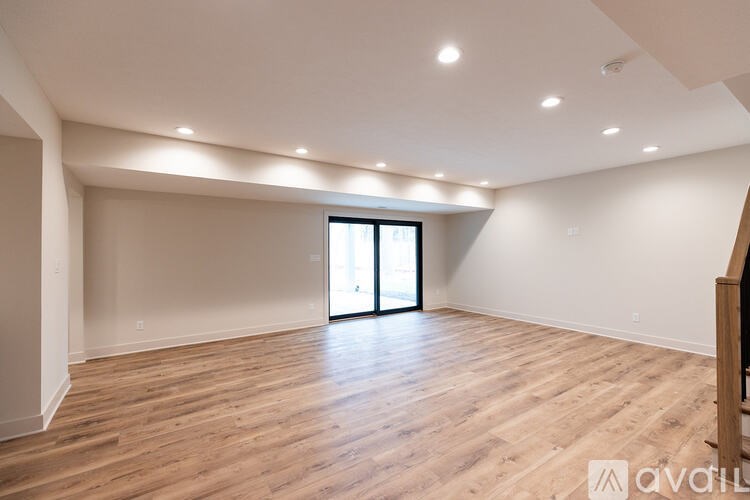 A spacious room with wooden flooring and a sliding glass door.