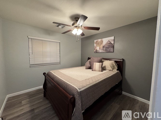 A bedroom with a bed, pillows, a ceiling fan, and a picture on the wall.