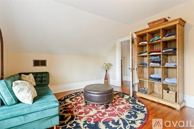 A room with a green sofa and a wooden cabinet with clothes.