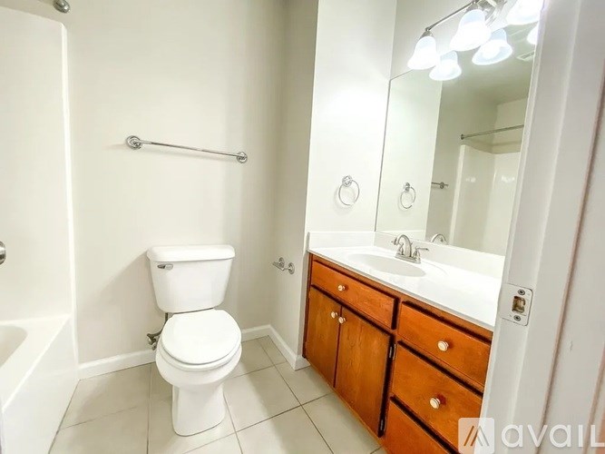 A white toilet sits in a bathroom with a white sink and wooden cabinets.