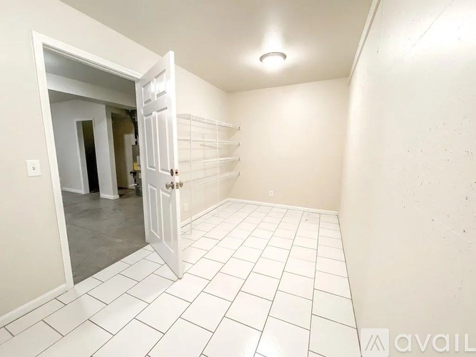 A white tiled room with a door open to another room.