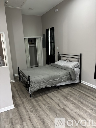 A bedroom with a bed, wooden floors, and a white wall.