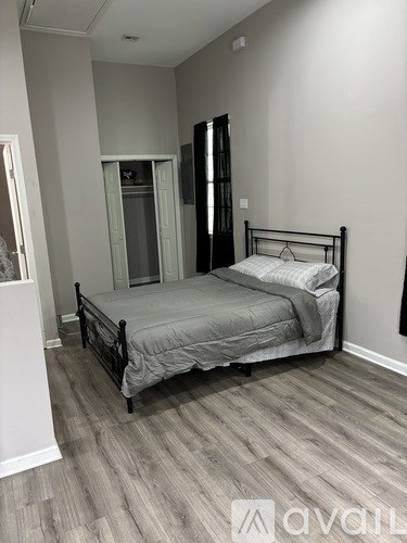 A bedroom with a bed, wooden floors, and a white wall.