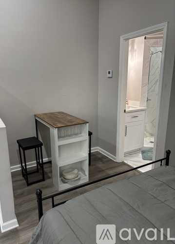 A bedroom with a bed, a small table with a chair, and a shelf with dishes.