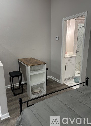 A bedroom with a bed, a small table with a chair, and a shelf with dishes.