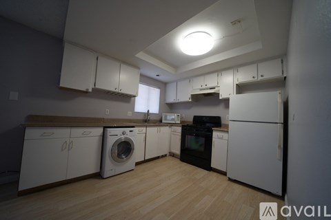 A kitchen with white cabinets and appliances, a wooden floor, and a skylight.