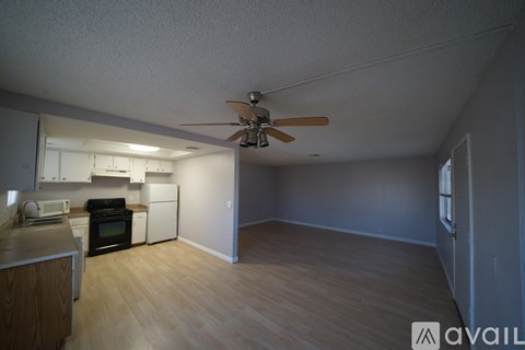 A room with a ceiling fan and a kitchen area with a microwave, oven, and refrigerator.