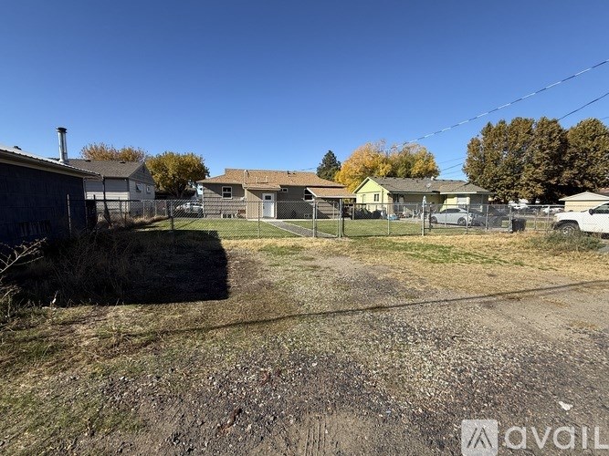 A dirt road leads to a fenced area with a house and trees in the background.