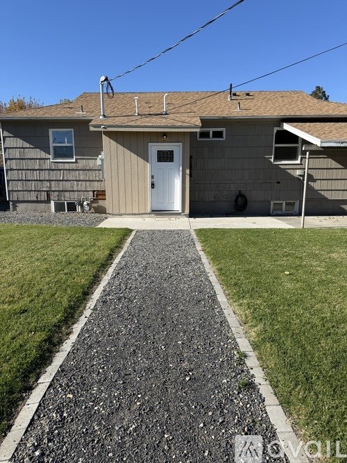 A house with a grey siding and a white door is surrounded by a gravel path.