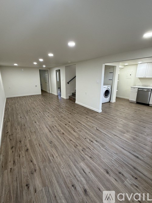 A spacious room with wooden flooring and a washer and dryer in the corner.