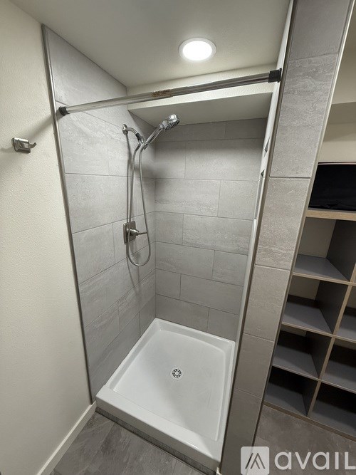 A shower area with a white tub and grey tiles.