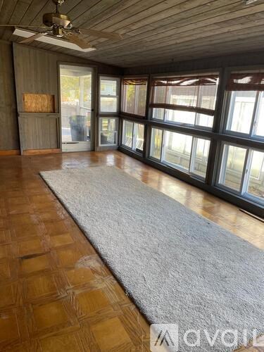 A room with wooden floors and a grey rug in front of a large window.
