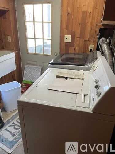 A white washing machine sits in a room with wooden walls.