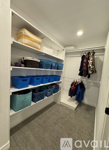A white closet with clothes hanging and baskets on shelves.