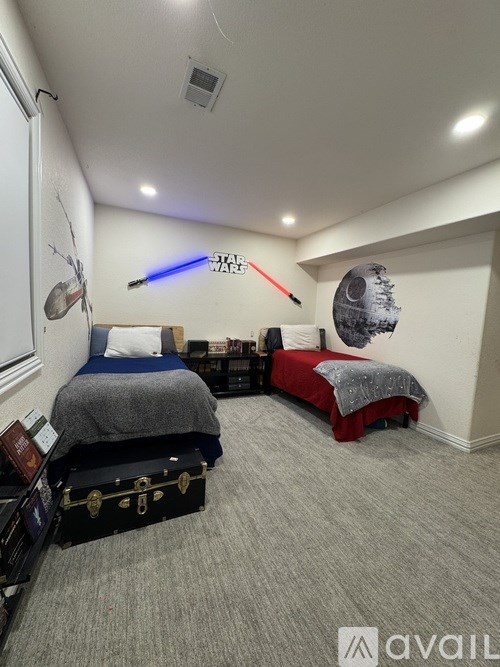 A bedroom with two beds, one with a grey bedspread and the other with a red bedspread, and a suitcase with a lock on it.