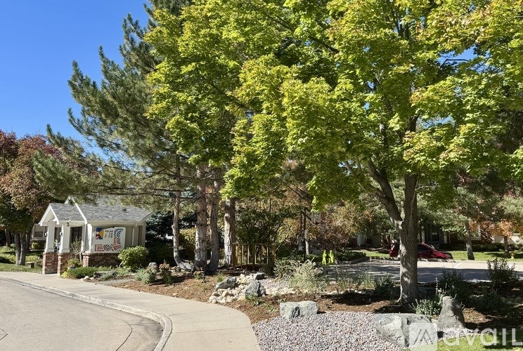 A small house with a porch is surrounded by trees and a sidewalk.