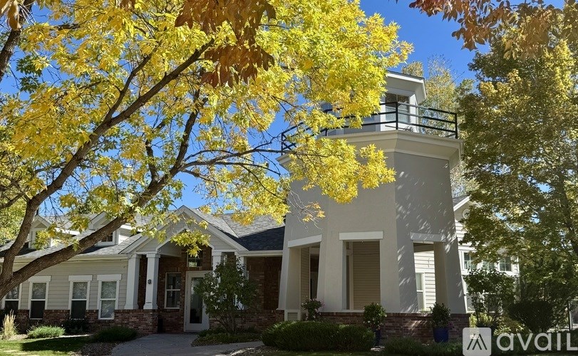 A house with a balcony and a tree with yellow leaves in front.