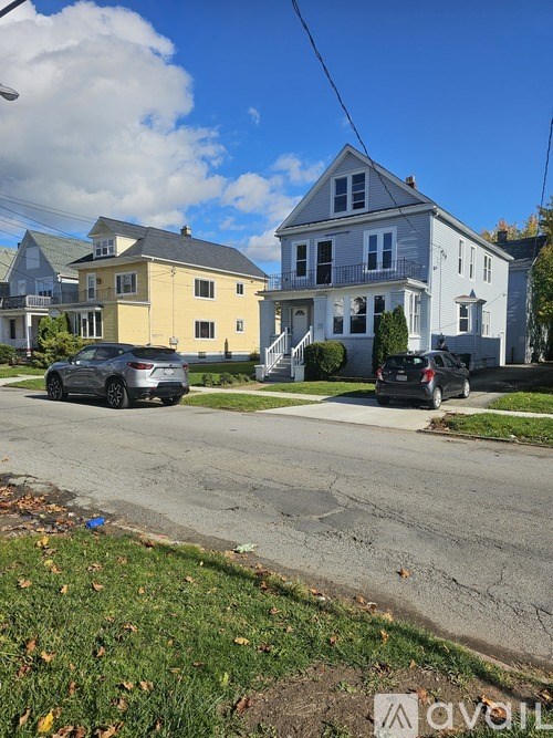 A street view with a yellow house on the left and a blue house on the right with cars parked in front.
