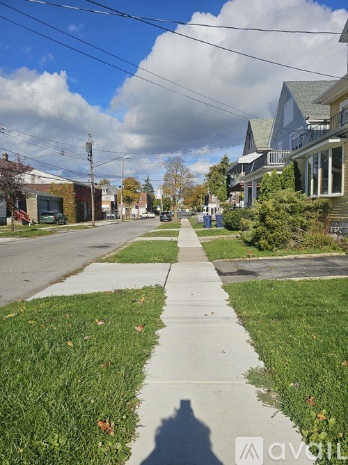 A sidewalk runs down the middle of a street with a house on the right.
