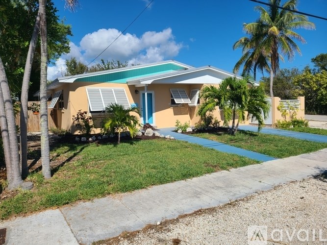 A house with a blue door and a green roof is surrounded by palm trees.