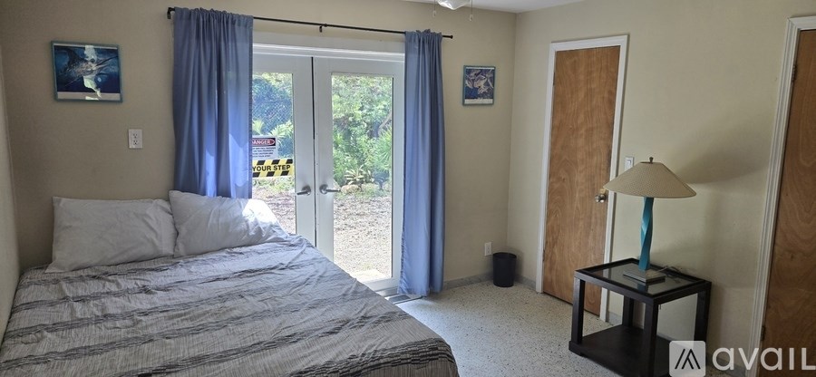 A bedroom with a bed, a nightstand with a lamp, and a door leading to a balcony.