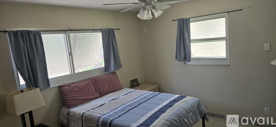 A bedroom with a bed, a ceiling fan, and a window with curtains.