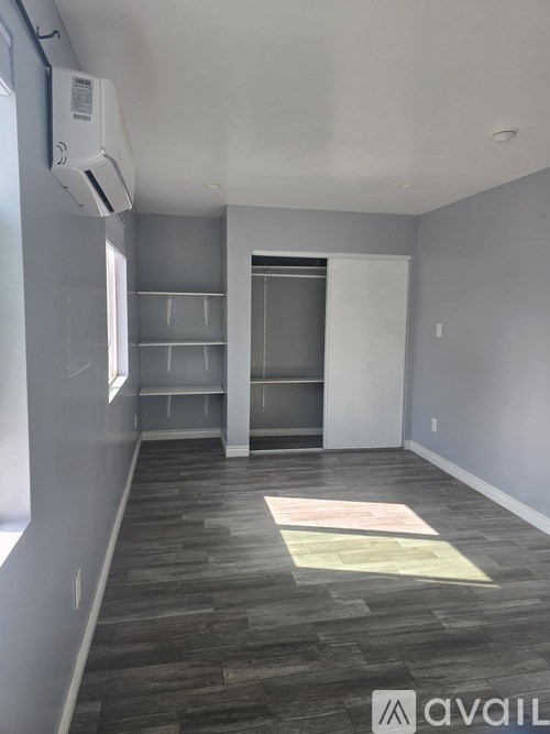 A room with grey walls and a wooden floor with a white door and shelves.