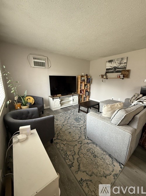 A living room with a grey couch, a black armchair, a white table, and a television.