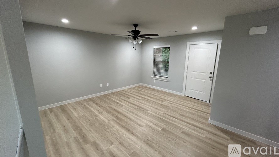 A room with a ceiling fan and lighting fixture, wooden flooring, and a door.
