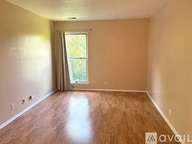 A room with wooden flooring and a window with a view of trees.