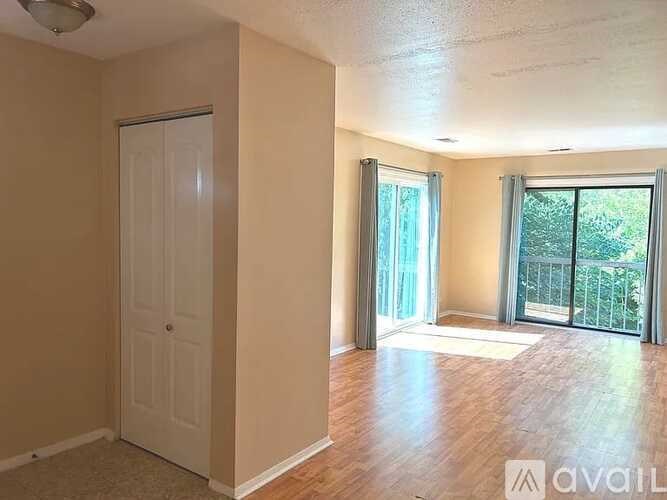 A room with a door, a window with a view of a balcony, and a wooden floor.