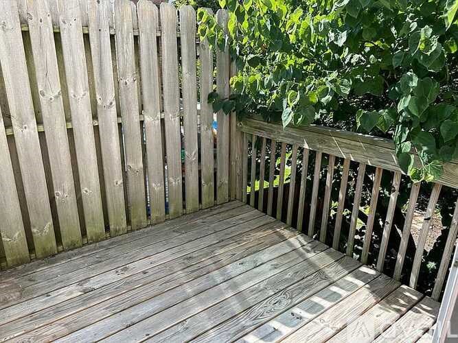 A wooden deck with a railing and a tree in the background.
