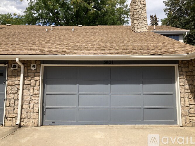 A house with a grey garage door and a stone wall.