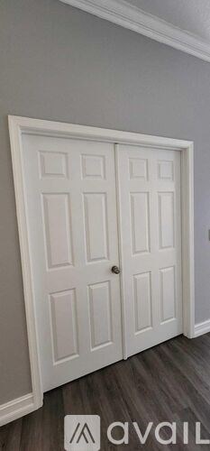 A white double door with a silver handle is set in a grey wall.