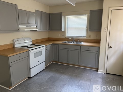 A kitchen with a white stove top oven and a sink with a window above it.