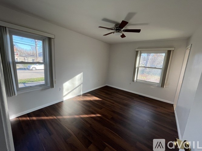 A room with a ceiling fan and two windows.