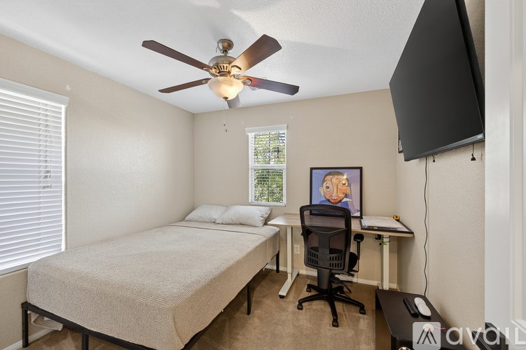 A bedroom with a bed, desk, and ceiling fan.