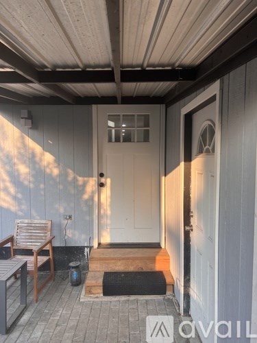 A wooden bench sits on a porch with a white door.