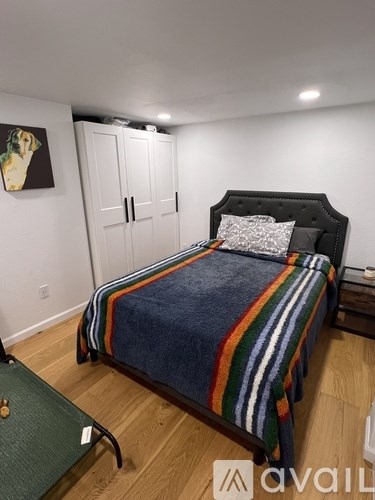A bedroom with a bed, a green ottoman, and a painting on the wall.