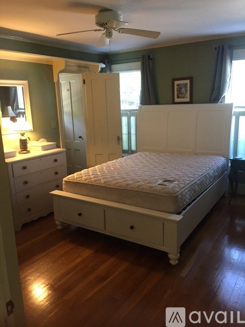 A white bed with a white mattress and a white dresser with a mirror and a lamp on it.