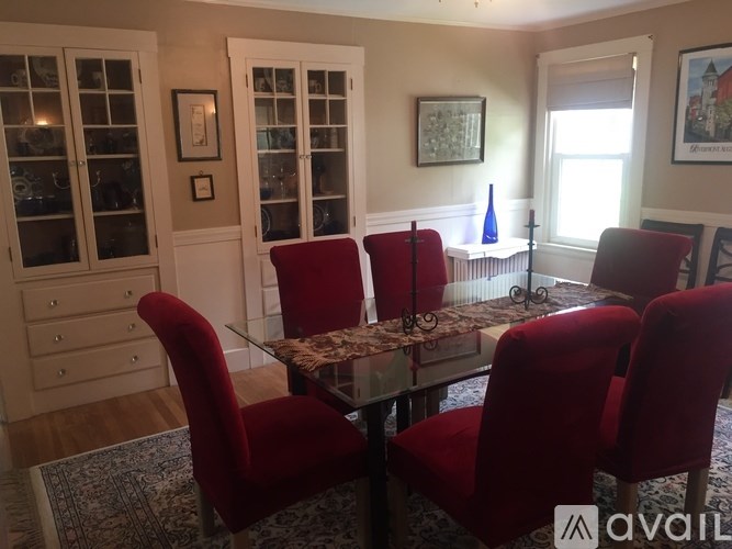 A dining room with a glass table and red chairs.